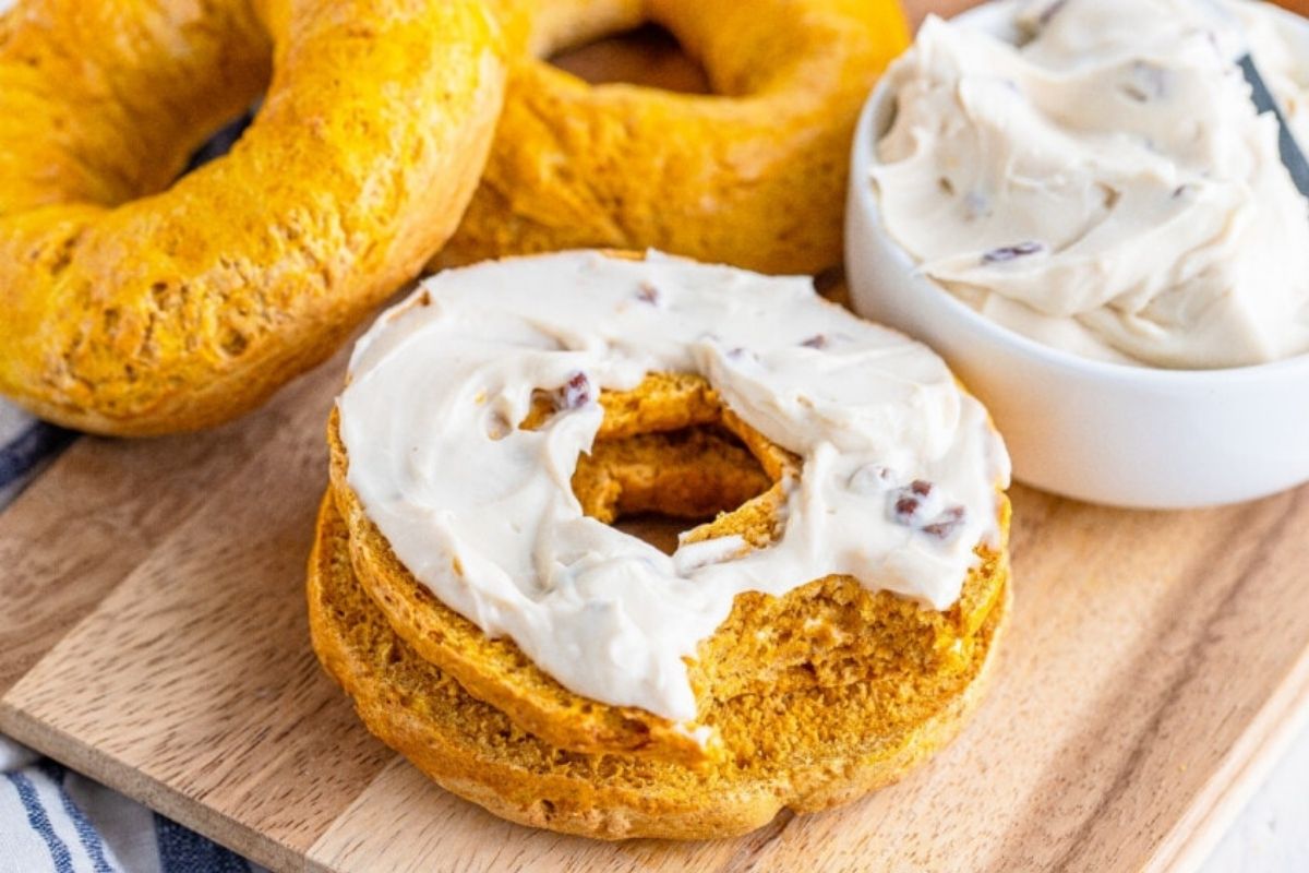 Bagels on cutting board with one covered in cream cheese.