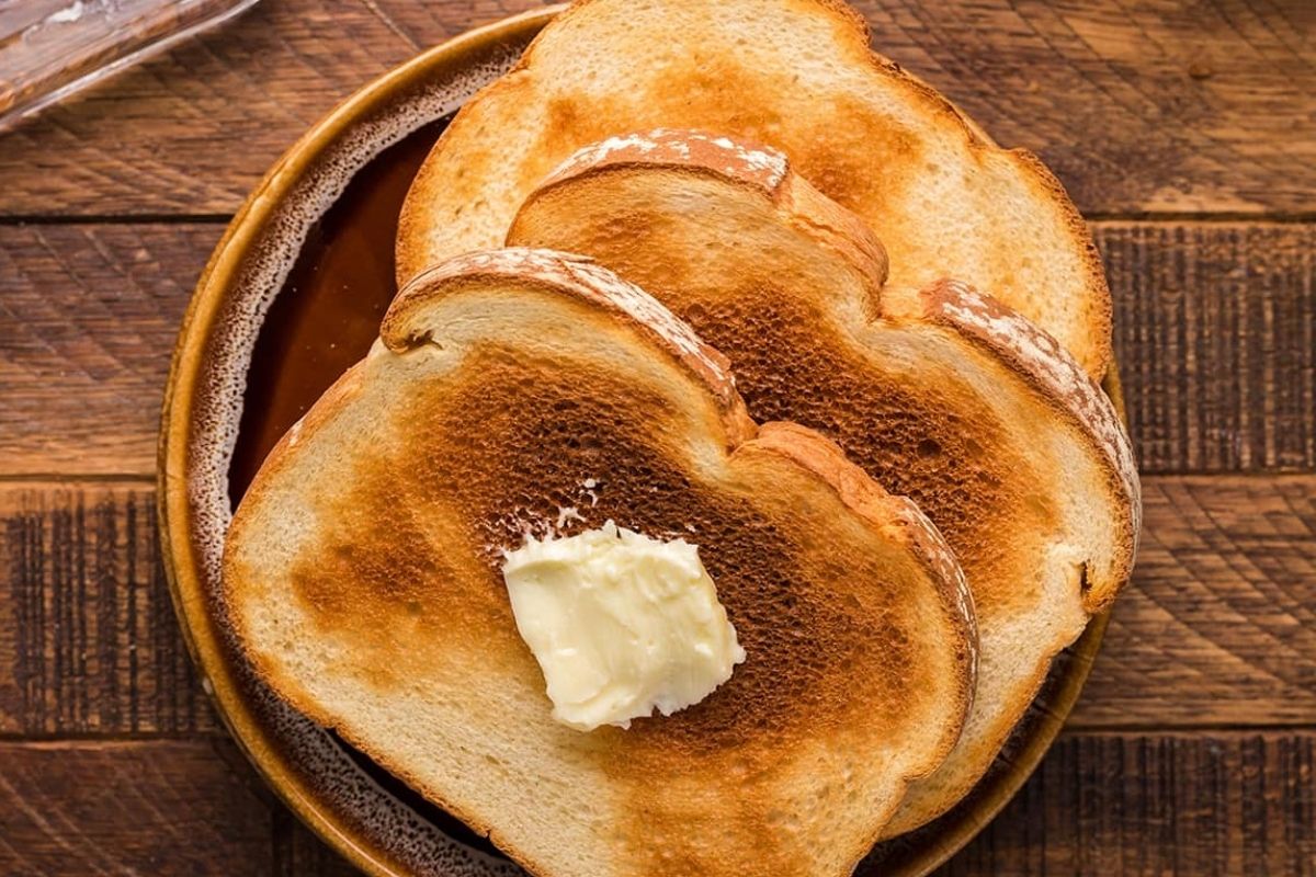 Three pieces of toast on a plate and the top slice has butter on it.