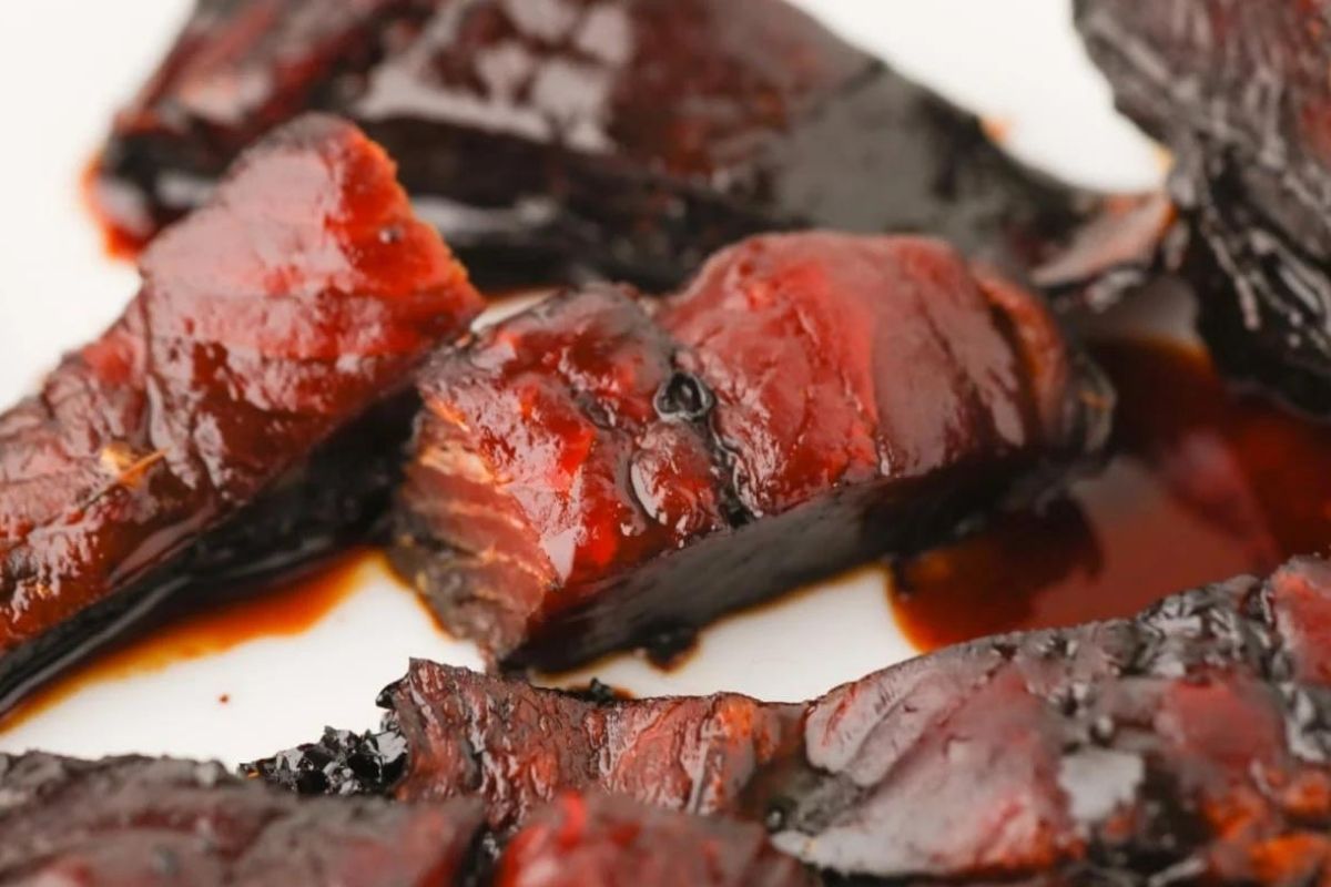 Close-up image of smoked barbecued ribs with a glossy sauce, highlighting the charred and caramelized surface on a white background.