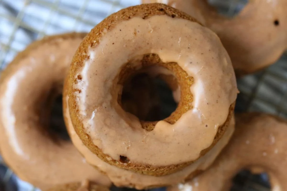 Close-up of a stack of glazed doughnuts on a cooling rack. The doughnuts have a light brown color and a glossy glaze.