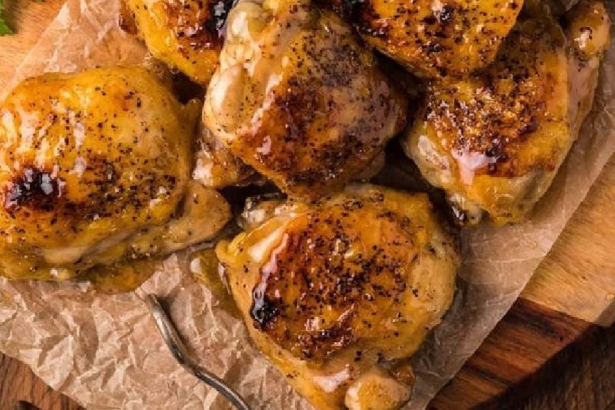 Several pieces of glazed, roasted chicken thighs on a piece of parchment paper with a small fork beside them, perfect for easy chicken thigh recipes.