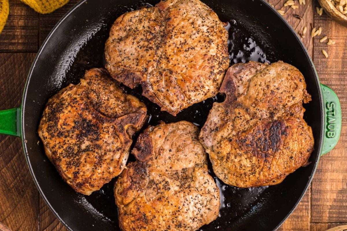 Four seasoned pork chops cooking in a cast iron skillet, viewed from above. This is one of the easy pork chop recipes to try at home.
