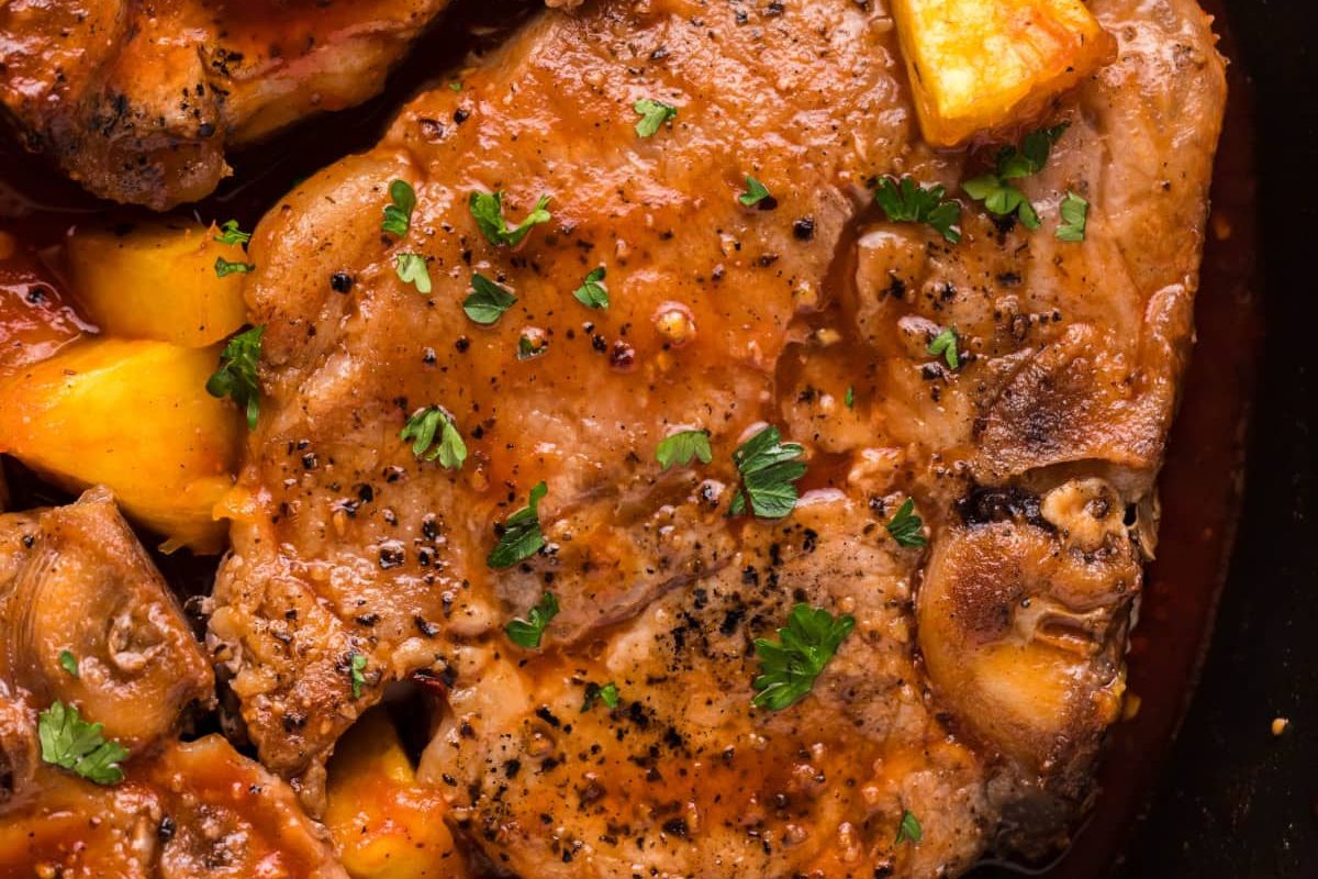 Close-up of a savory pork chop dish with herbs, spices, and slices of peach in a dark baking dish, ideal for easy pork chop recipes.