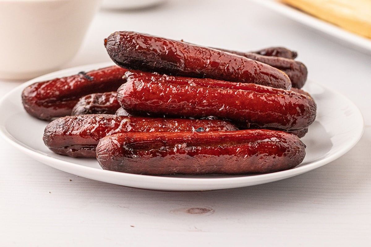 A white plate is filled with several grilled sausages, inspired by classic smoker recipes.
