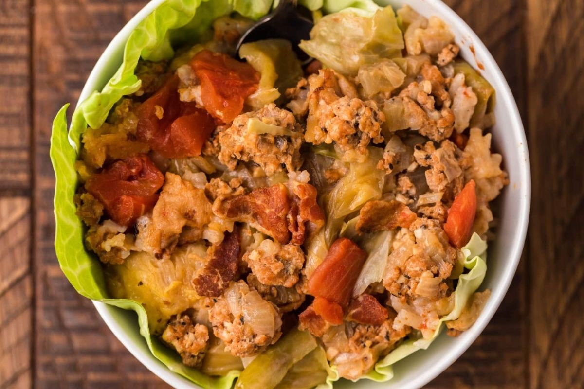 A bowl of stuffed cabbage rolls with a mix of chopped cabbage, ground meat, tomatoes, and rice, simmered to perfection in a slow cooker on a wooden surface.