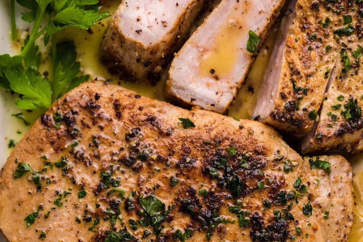 Close-up of seasoned and cooked pork chops garnished with herbs, served with gravy and a side of fresh parsley. Perfect for family meals, these easy pork chop recipes are sure to impress.