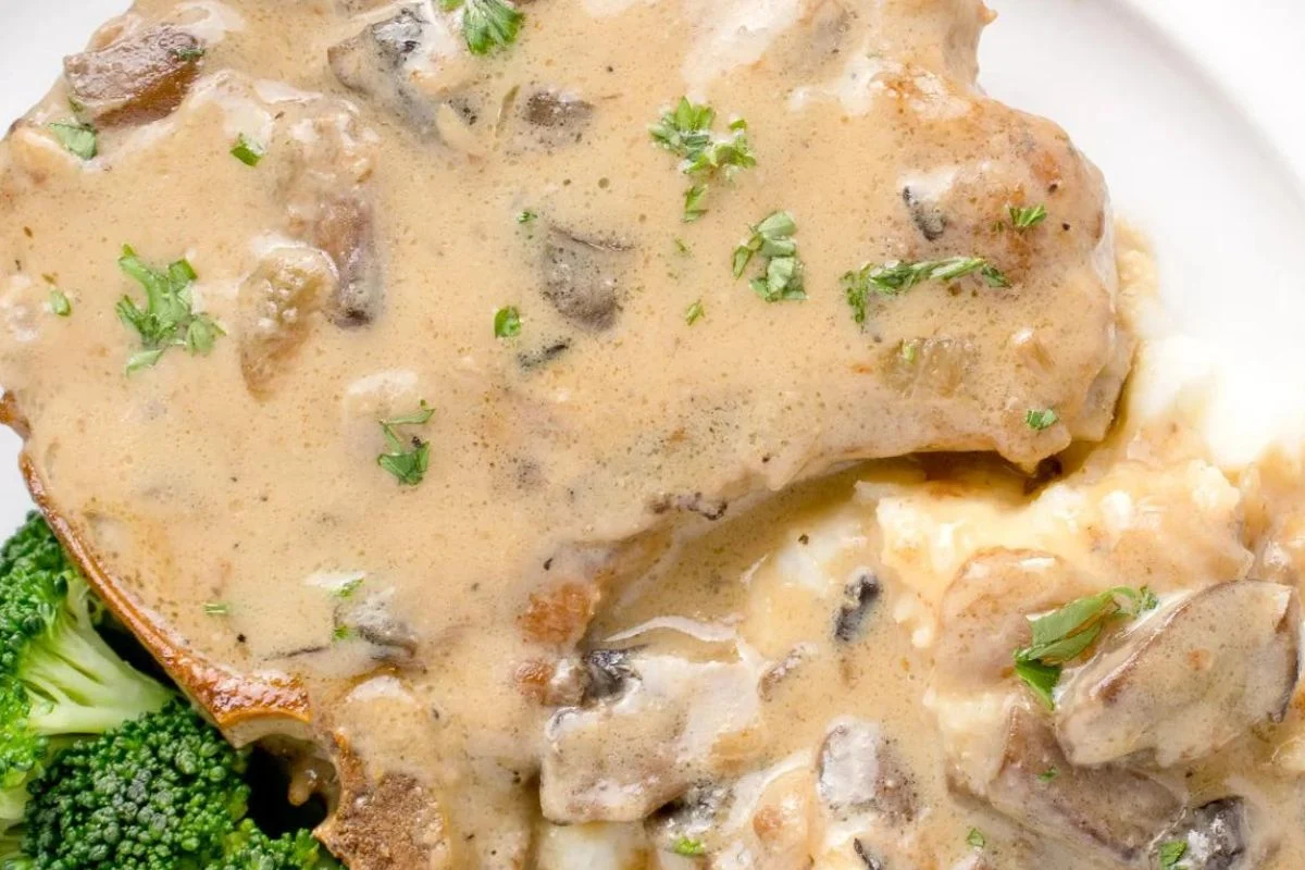 Easy pork chop with creamy mushroom sauce, served alongside mashed potatoes and broccoli, garnished with parsley.