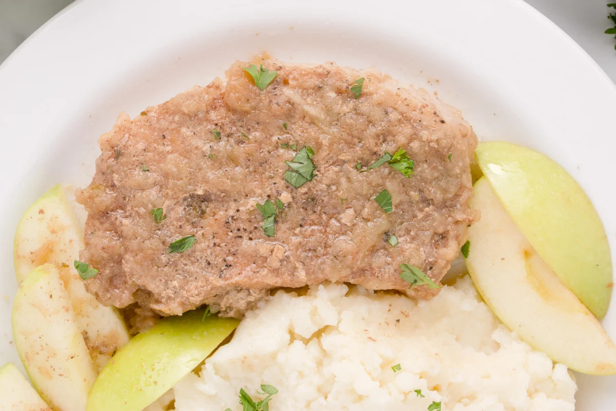 Slow Cooker Pork Chops With Apples on a white plate with mashed potatoes.