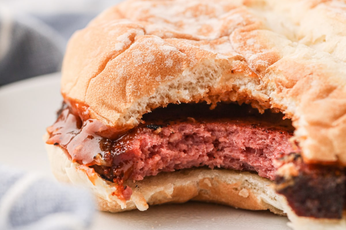 Close-up of a partially bitten sandwich with a thick patty and barbecue sauce in a soft, toasted bun, perfect for smoked dinners or served alongside your favorite sides.