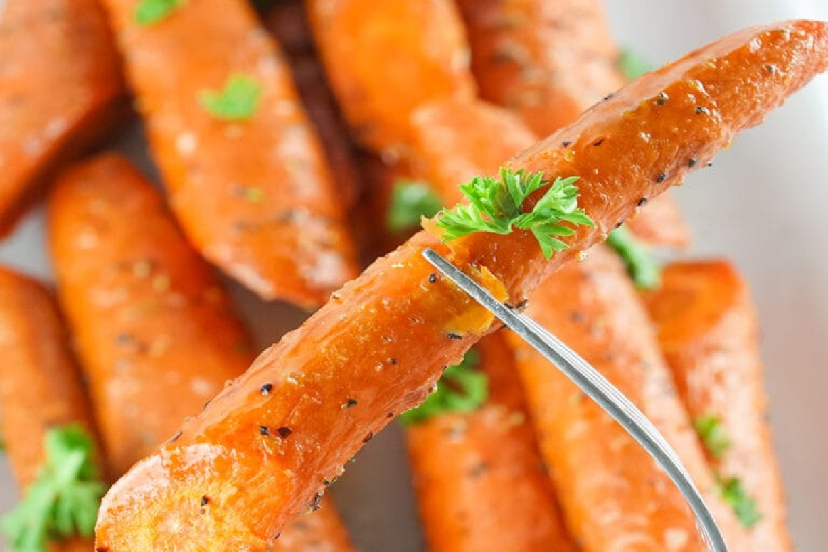 A close-up of a fork holding a roasted carrot garnished with parsley, reminiscent of smoker recipes. Several roasted carrots are visible in the background.