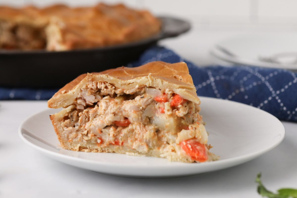 A slice of smoked chicken pot pie on a white plate, with the whole pie visible in the background.