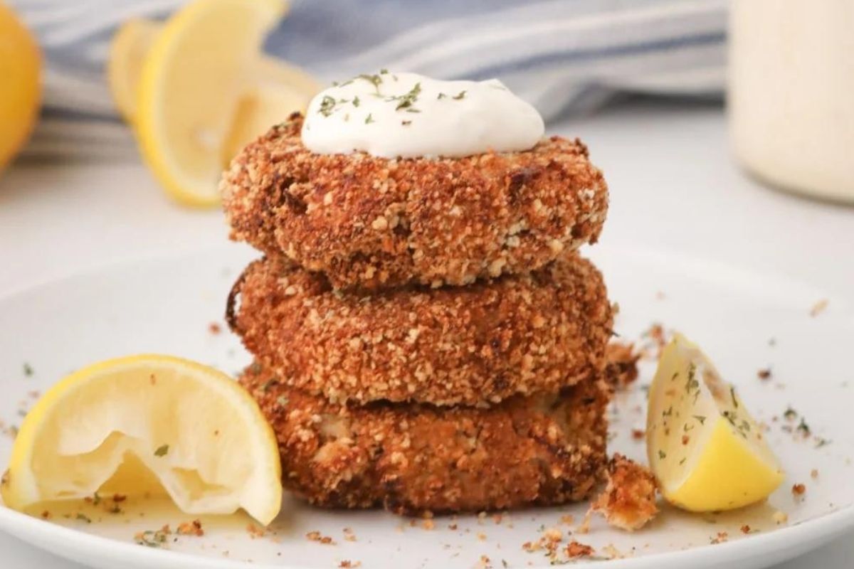 A stack of three crispy cakes on a white plate, garnished with a dollop of tartar sauce and lemon wedges on the side, perfect for a light meal after reviewing the