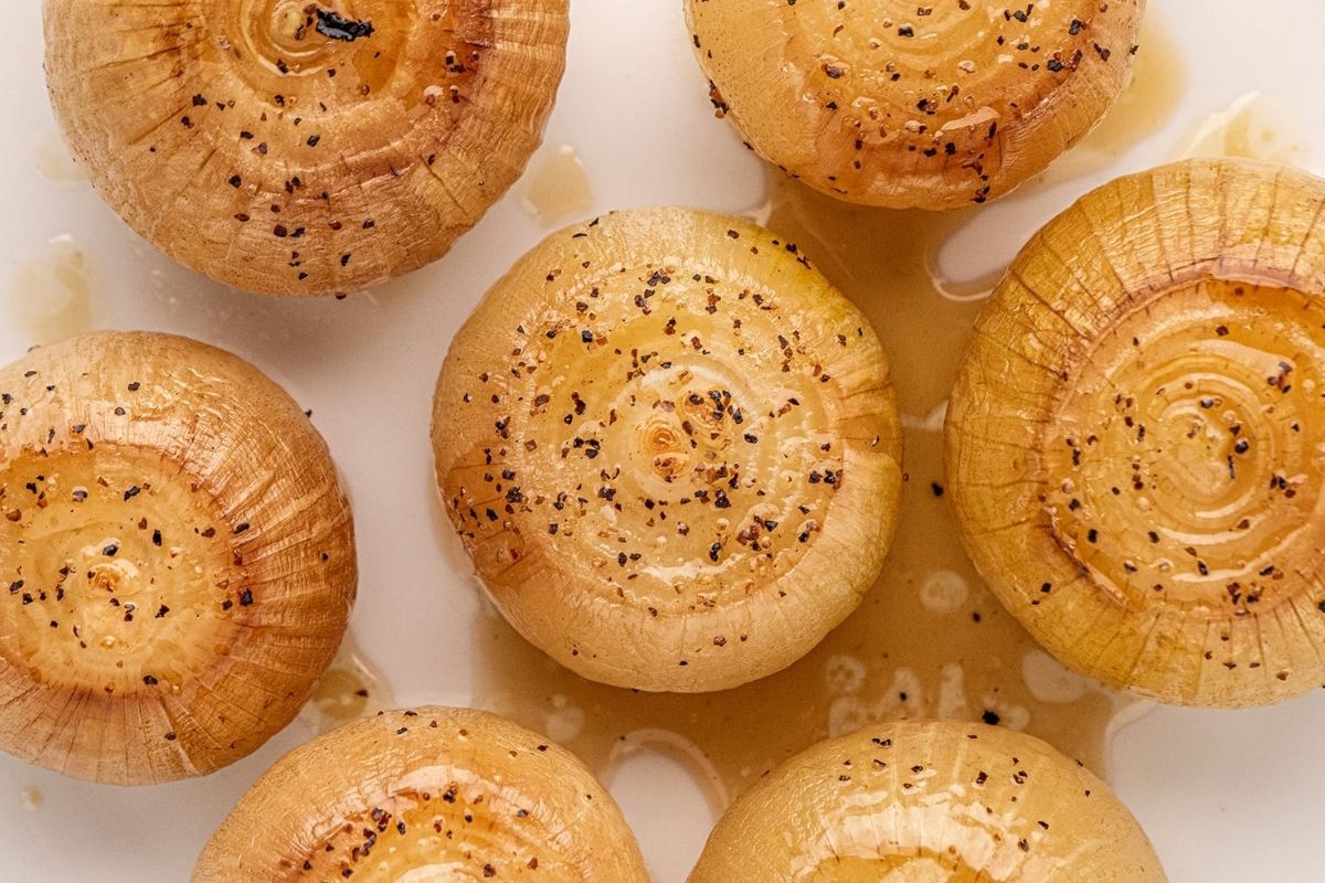 Roasted onions with seasonings and olive oil, arranged on a white surface, perfect for incorporating into your smoker recipes.