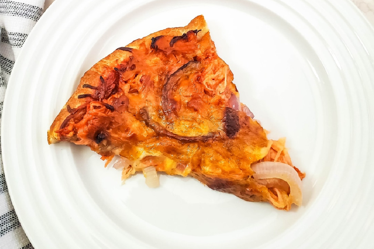 A slice of pizza with visibly burnt edges, reminiscent of smoked recipes, is topped with melted cheese and onions on a white plate.