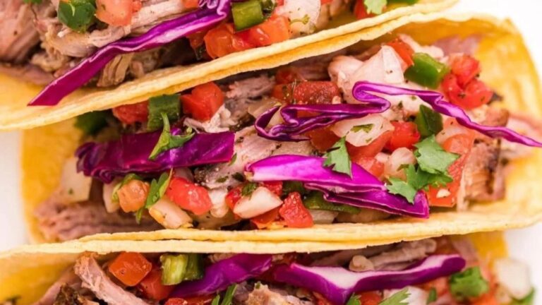 Three tacos filled with smoked shredded meat, diced tomatoes, red cabbage, and cilantro in crispy yellow corn shells.