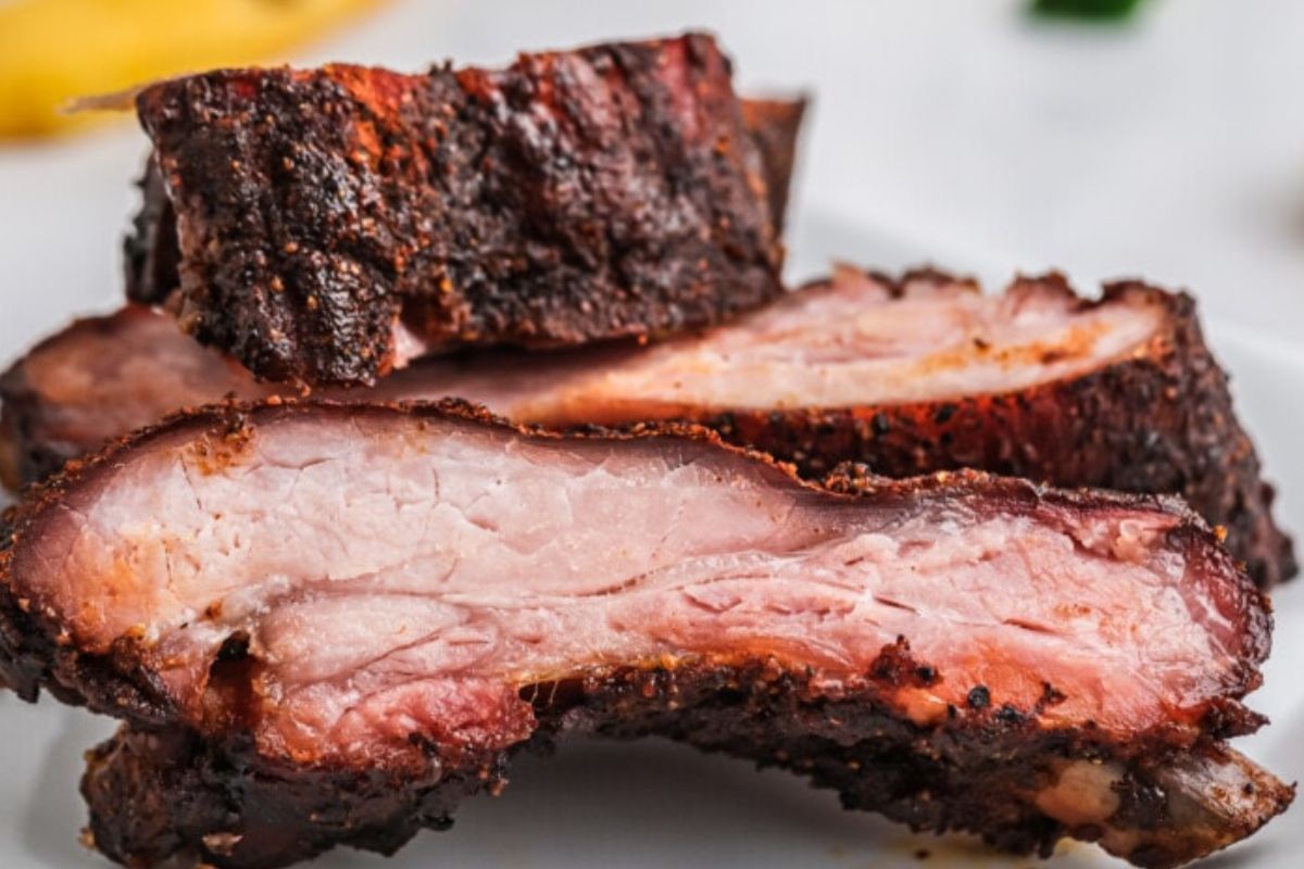 Close-up of sliced, grilled pork ribs on a plate. The meat is tender and juicy with a well-cooked, slightly charred exterior, perfect for finger-lickin' enjoyment. This mouth-watering dish is ideal for anyone searching for delicious ribs recipes.
