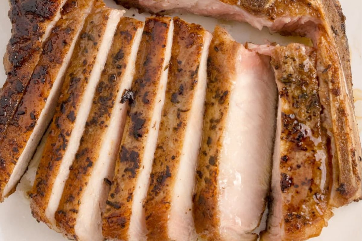 Sliced pork chop on a white plate, showing a juicy pink center and well-seasoned crust.