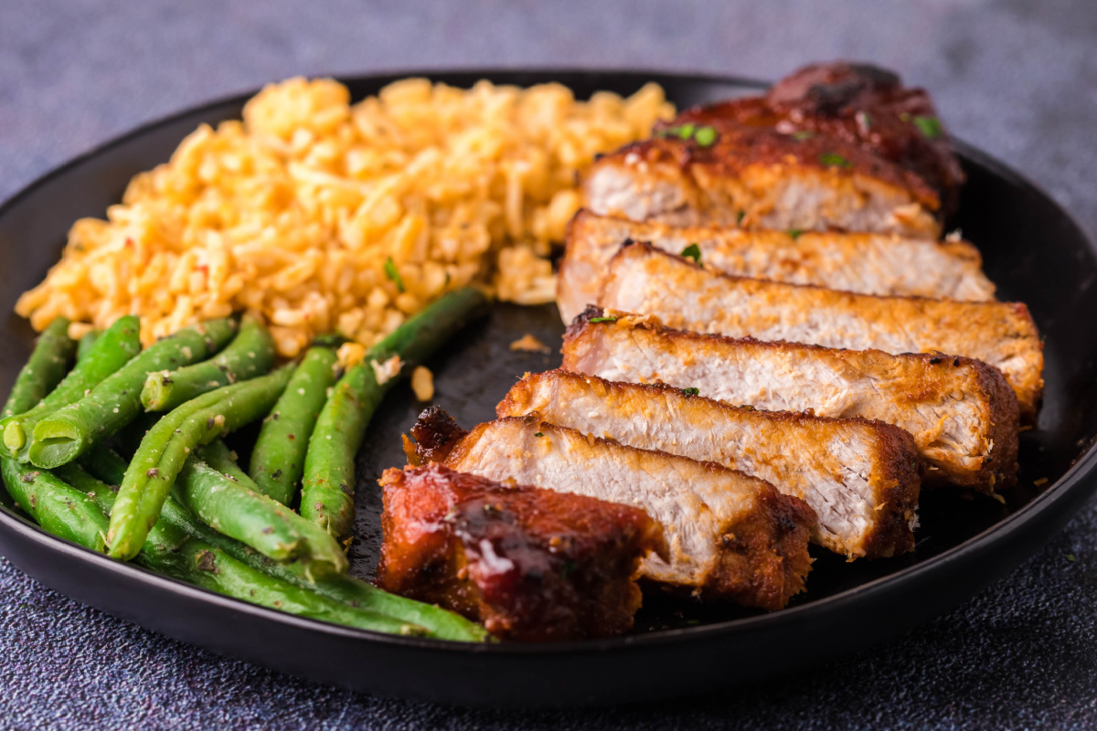 A plate with sliced pork chops, green beans, and a serving of mac and cheese makes for one of the perfect family meals, showcasing easy pork chop recipes that everyone will love.